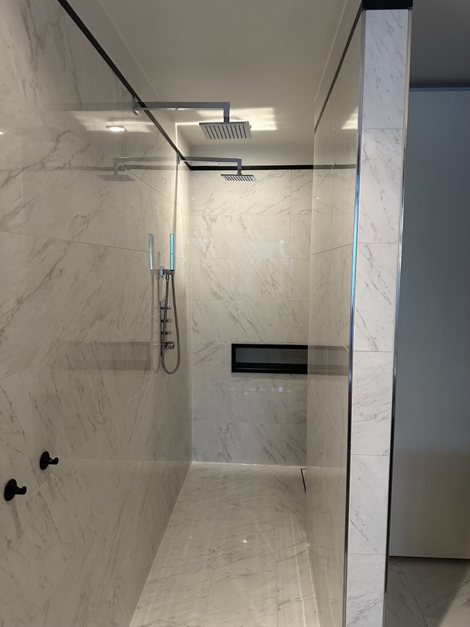 Walk-in shower with a rain shower head in white marble