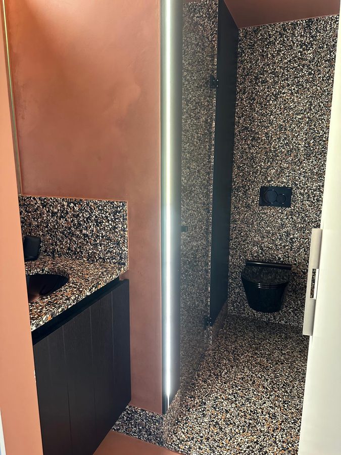 Terrazzo toilet and washbasin with terracotta walls and a lit mirror