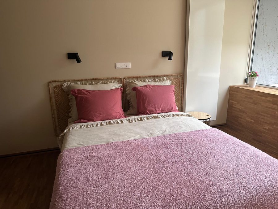 Double bed with a pink bedspread and rattan headboard by the window