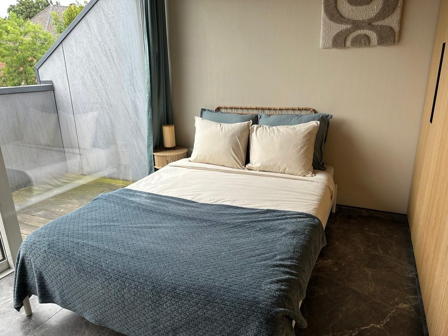 Double bed with a teal bedspread and rattan headboard beside the terrace window