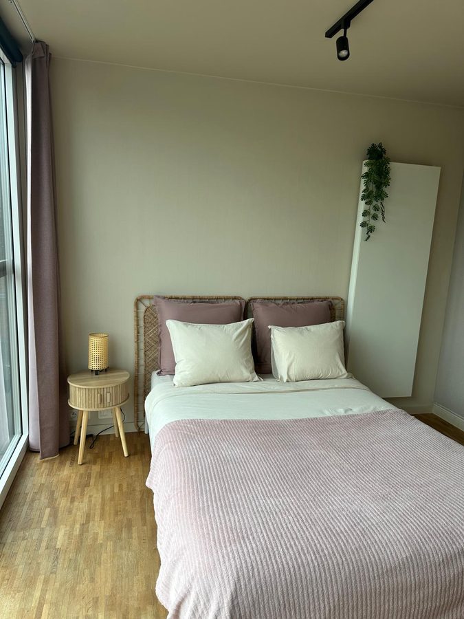 Bed with dusty pink cushions, a rattan headboard and a round nightstand